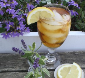 Photo of a glass of iced tea next to a planter with floweres and Lavender and mint in a small vase