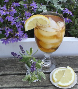 Photo of a glass of iced tea next to a planter with floweres and Lavender and mint in a small vase