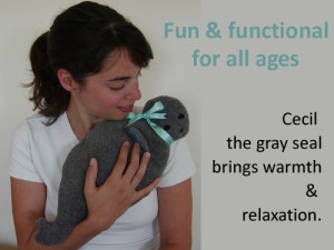 Woman using seal microwave heating pad to relax sore muscles, words say Fun & functional for all ages, the Gray Seal brings warmth & relaxation