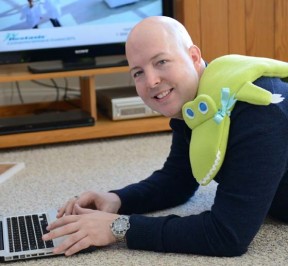 man realing with alligator neck warmer while watching TV and using laptop