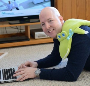 man realing with alligator neck warmer while watching TV and using laptop