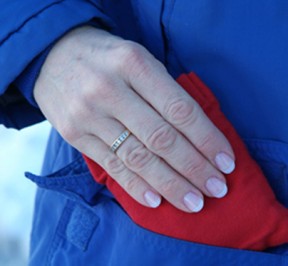 Small, red microwave hand warmer being inserted into a woman's coat pocket