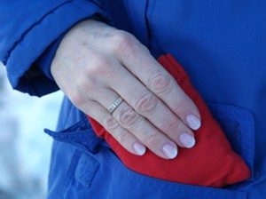 Small, red microwave hand warmer being inserted into a woman's coat pocket