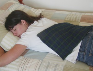 Woman relaxing sore back muscles with a microwaveable back warmer in Tartan plaid with a washable cover