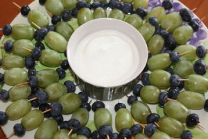 Green grapes and blueberries on toothpicks arranged around a plate with yogurt dip in the center