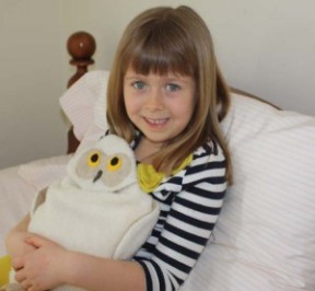 Girl using Snowy Owl microwave heating pad to ease a tummy ache