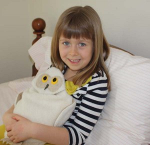 Girl using Snowy Owl microwave heating pad to ease a tummy ache