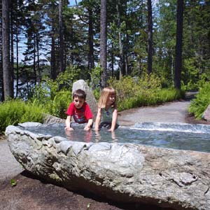 Two kids playing in a pool of water at the mediation garden at the Coastal Maine Botanical Gardens in Boothbay, Maine