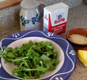 Arugula salad for one with salt & pepper shakers, half a lemon, and grated parmesan