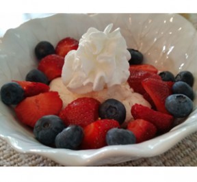 Fresh blueberries and strawberries surround ing a baked meringue with a dollop of whipped cream on top