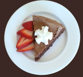 Wedge of Flourless Chocolate Cake with sliced strawberries on the side and a little whipped cream on top