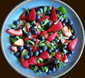 Fresh Blueberries_ strawberries_ cantaloupe_ and basil on fresh baby greens in a blue pottery salad bowl