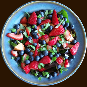 Fresh Blueberries_ strawberries_ cantaloupe_ and basil on fresh baby greens in a blue pottery salad bowl